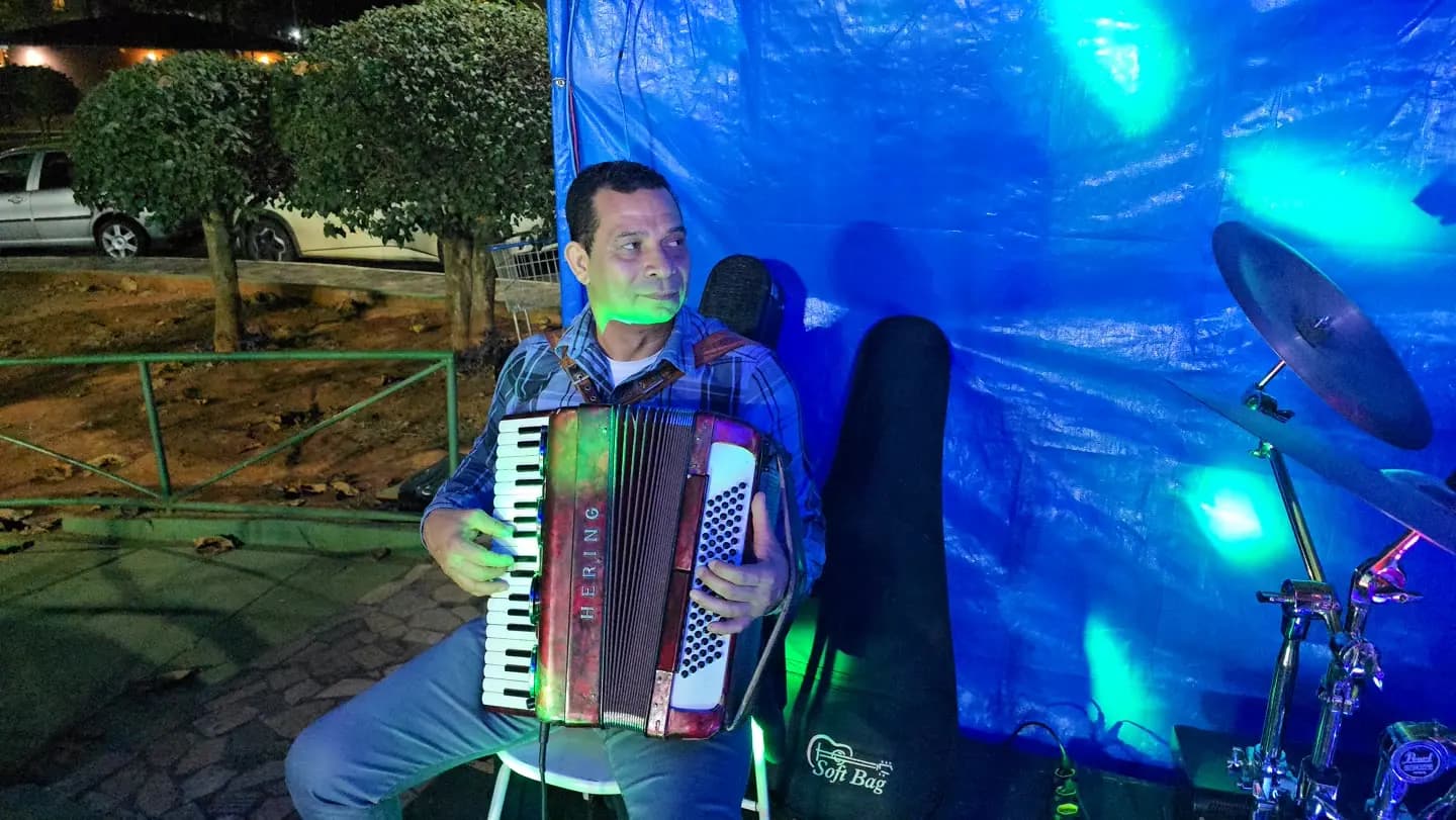 Sanfoneiro de camisa xadrez tocando acordeão sob uma lona azul.