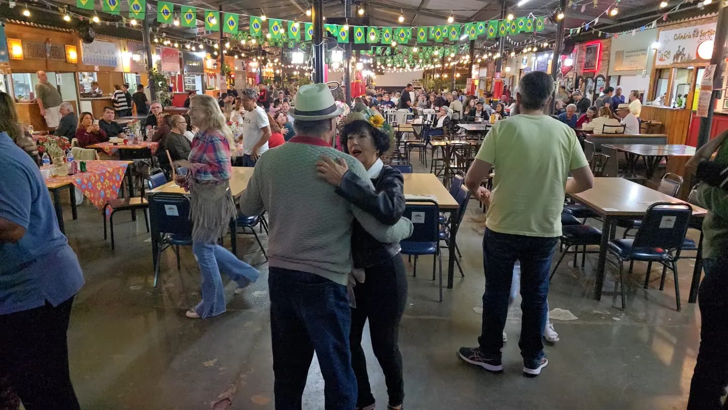 Casal dançando em primeiro plano num salão cheio, com o palco ao fundo.