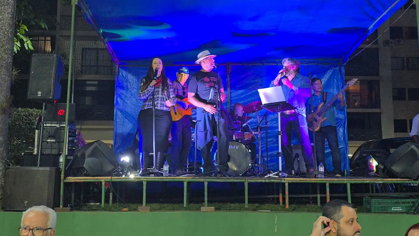 Banda inteira num palco azul de festa junina, à noite.